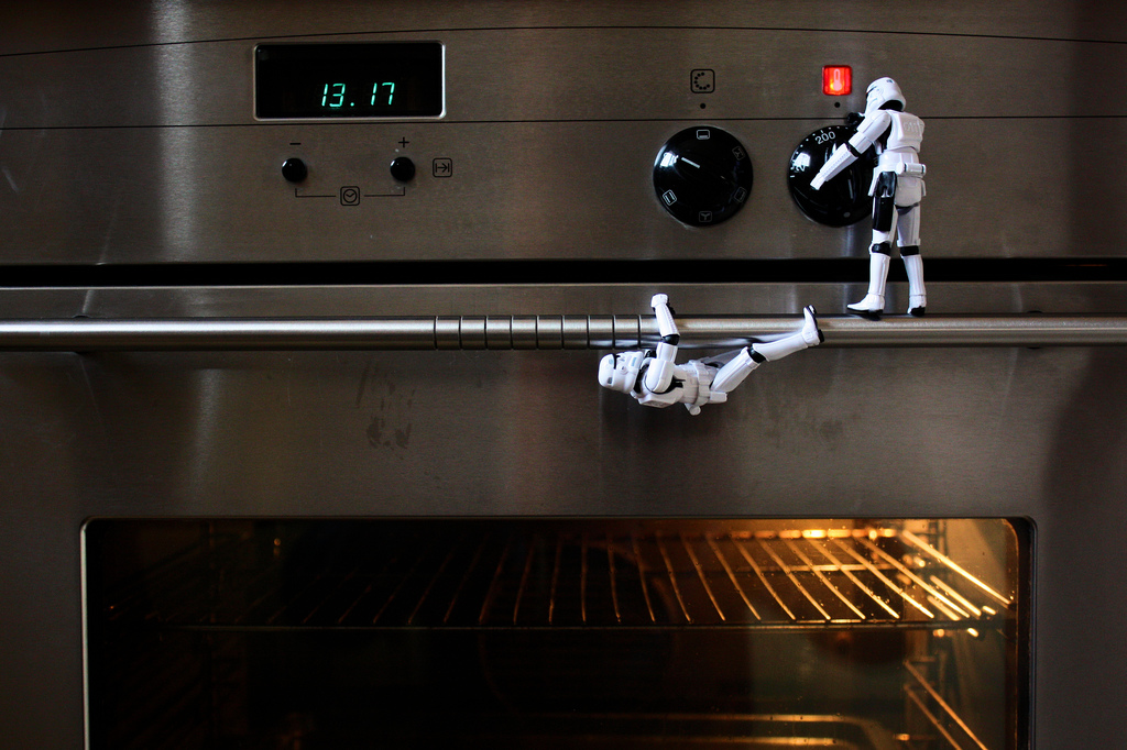 "Stormtrooper figurines operating a regular kitchen oven, one hanging in the door handle, and the other appearing to turn a knob."